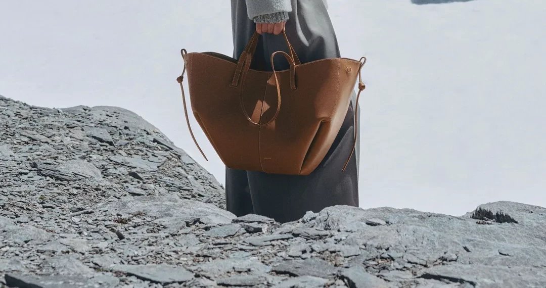 A tan leather tote carried across a snowy, rocky mountainside